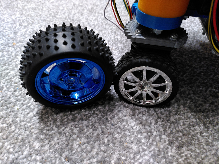 A detail view of a robot with small wheels next to larger spiked tires.