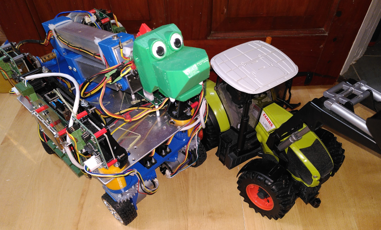 A four wheeled robot with dragon head next to a toy tractor.