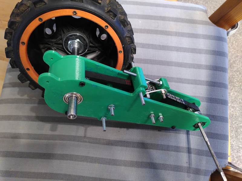 An assembly of green 3D printed parts with a drive belt and large wheel.