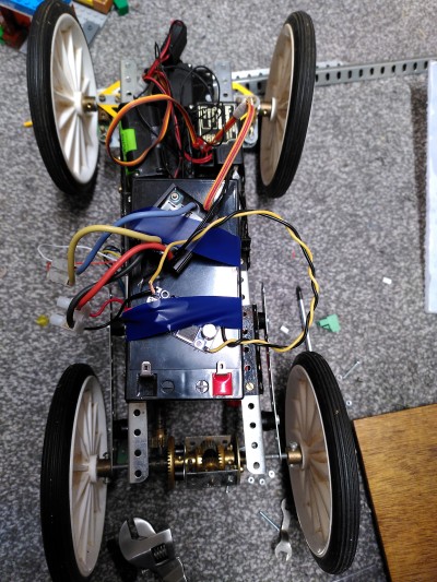 A crude Meccano chassis with battery and electronics taped to it.