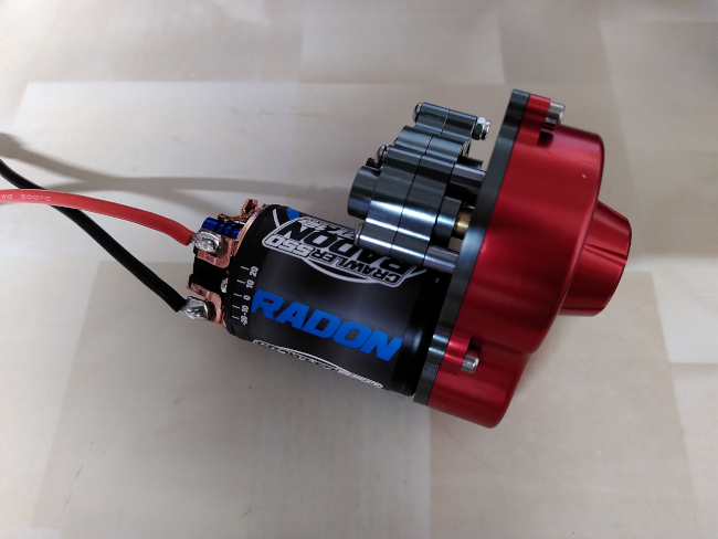 A shiny red gearbox with a chunky RC car motor attached.