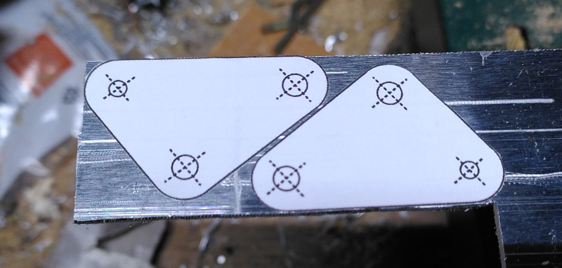 A piece of aluminium with two triangular stickers with drill marks on them.